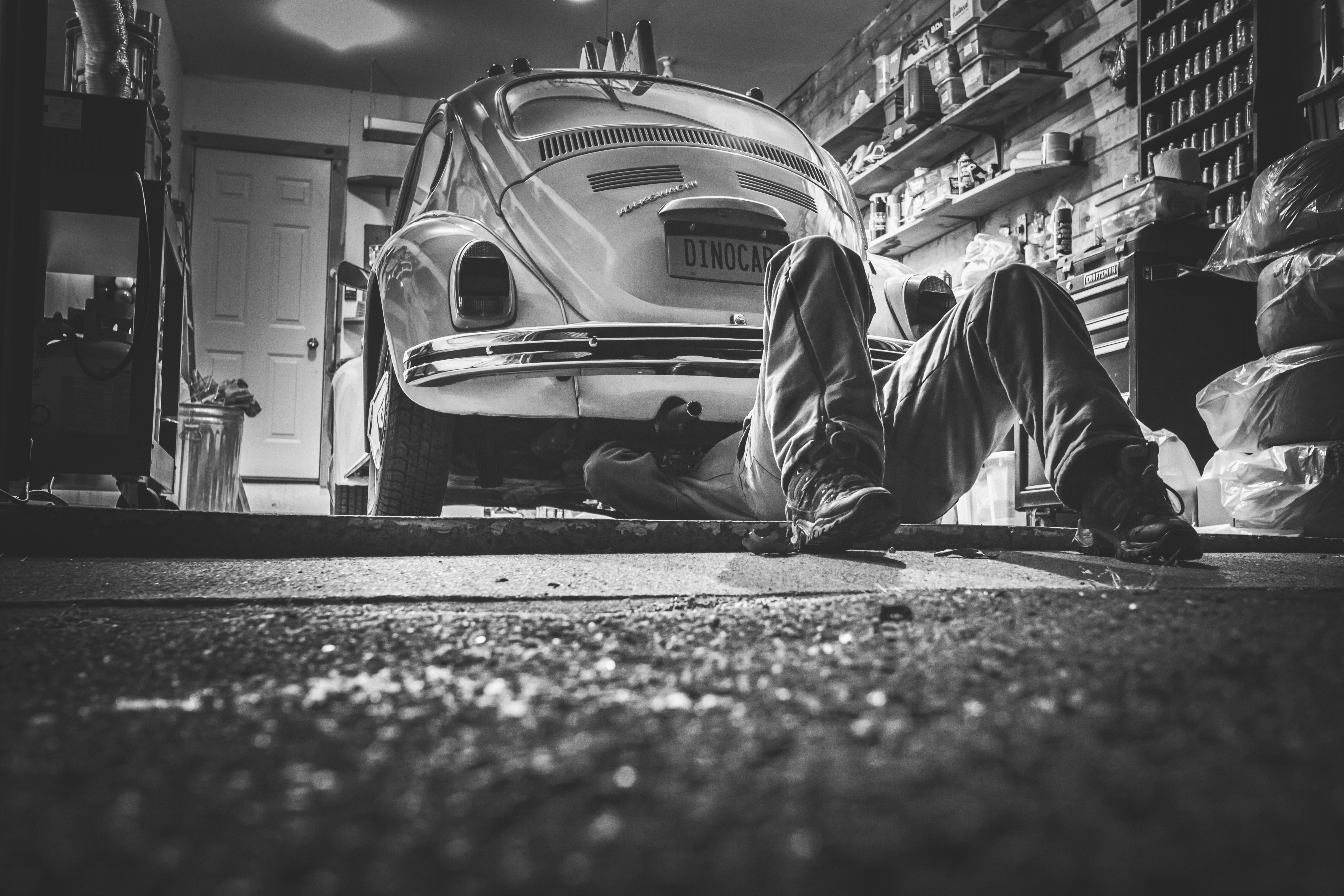 black and white image of mechanic working under a Volkswagon Bug