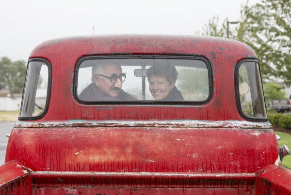 This is a picture of a couple looking behind them while riding in an old red car on a blog explaining the difference between a credit union vs. bank