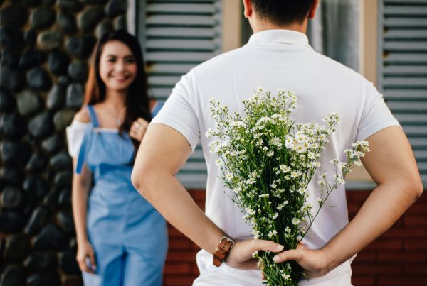 A person holding a bouquet of flowers behind their back while another person looks and smiles at them. This blog is about credit union loans.